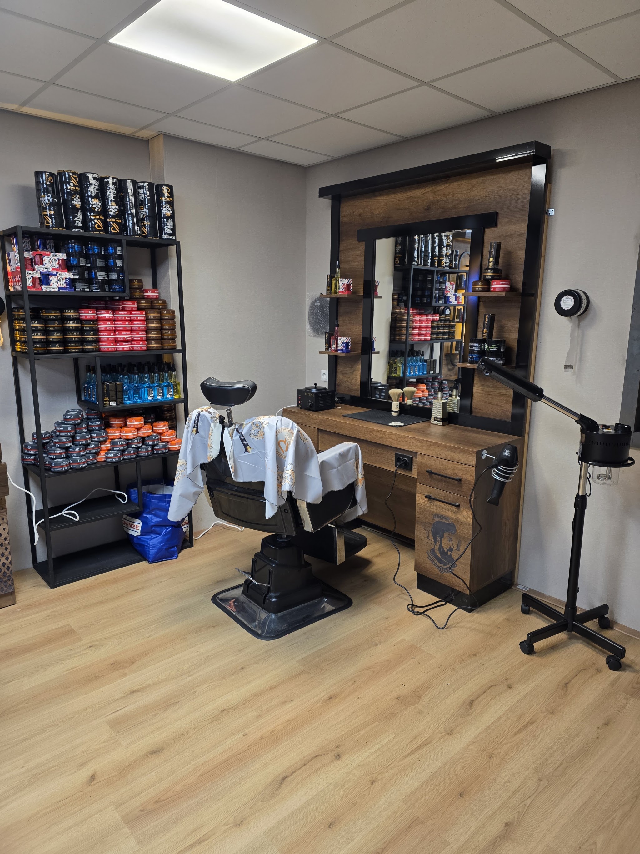 Een barberstoel bij een spiegel met verlichting, met rekken vol haarproducten ernaast
