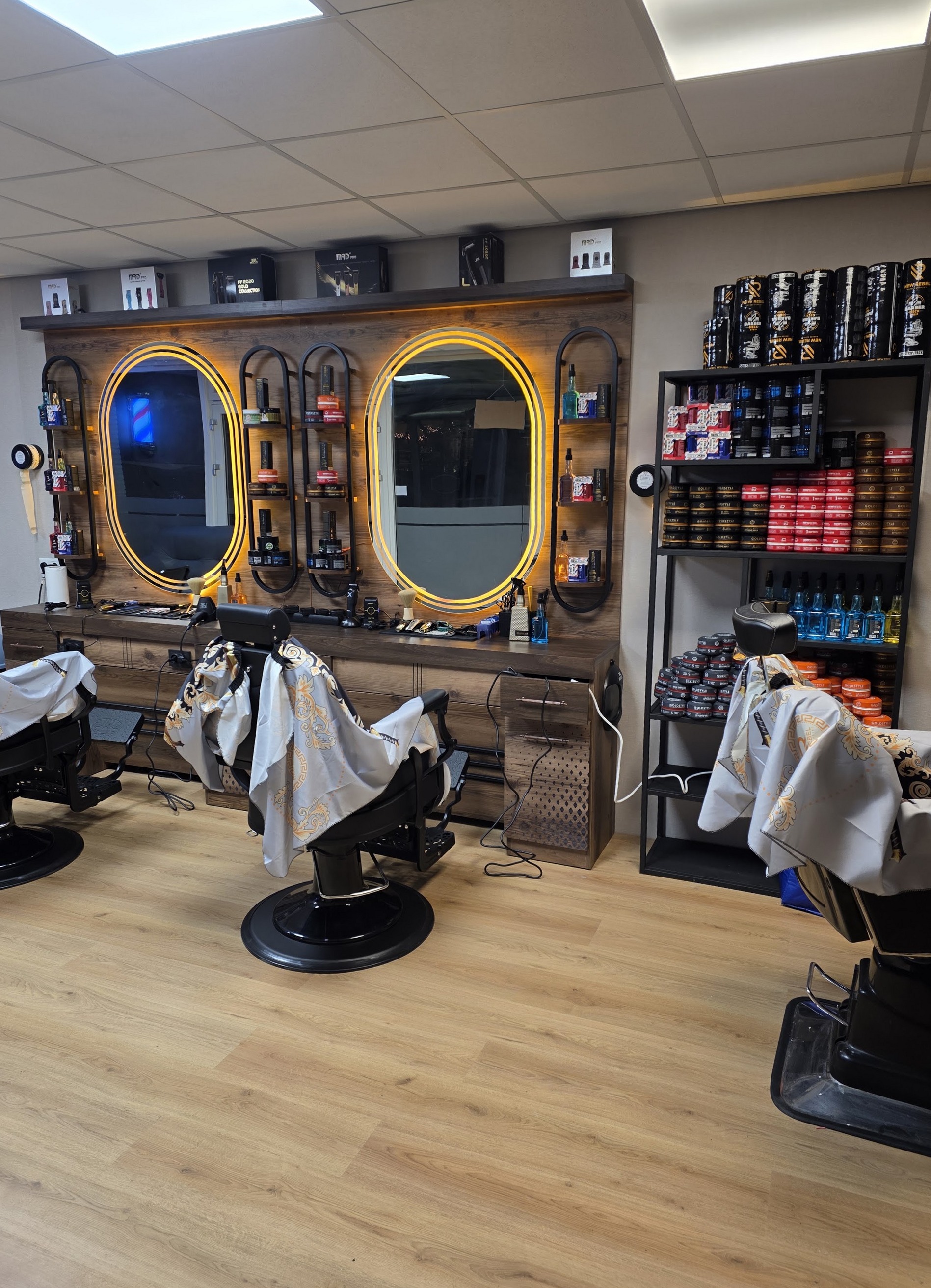 Drie barberstoelen voor de goudverlichte ovale spiegels in Goor’s Barbershop